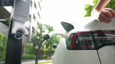 Yavaş çekim çift yazın yeşil sürdürülebilir şehir açık bahçesinde elektrikli araba şarj ile seyahat elektrikli aracın temiz yeniden şarj edilebilir enerjisi için kentsel sürdürülebilirlik yaşam tarzı olarak