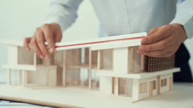 Profesyonel erkek mimar ev modelinin uzunluğunu ölçmek için cetvel kullanırken, beyaz tenli genç meslektaşı ev modeliyle toplantı masasındaki verileri analiz etmek için dizüstü bilgisayar kullanıyor. Tertemiz..