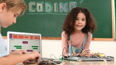 Kız tornavida kullanarak elektronik tahtayı tamir ederken ayakta duruyor. Amerikalı öğrenci ve beyaz çocuk elektrik sistemini denetlemek için birlikte çalışıyorlar. Gemide çalışan meraklı çocuklar. Pedagoji.