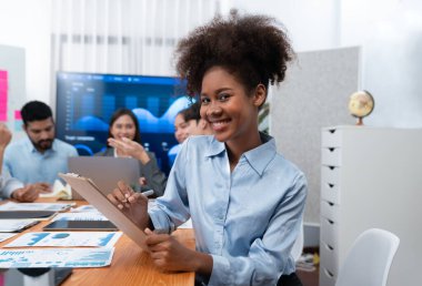 Bir grup ofis çalışanı ile birlikte arka planda ekranda gösterim paneliyle buluşan mutlu Afrikalı genç bir iş kadını portresi. Takım toplantısında kendine güveni tam bir ofis hanımı. Uyum