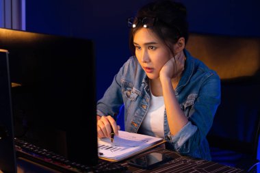 Genç, Asyalı yaratıcı bir kadının satış hedefi raporundan elde ettiği karı analiz etmesi, e-posta ile iş piyasası raporlarını karşılaştırması, gece neon ışığı altında not defterine not yazması. Taktik.