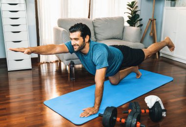 Spor giyimli esnek ve becerikli bir adam evde egzersiz paspası üzerinde meditasyon pozisyonunda yoga yapıyor. Huzurlu ve huzurlu bir yoga yaşam tarzı..