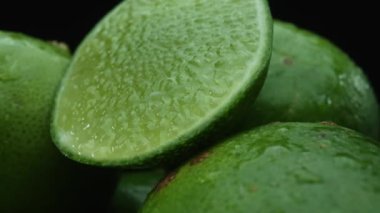 Limon dilimleri titizlikle bir yığın halinde, siyah arkaplana göre dizilmiş. Her bir kireç dilimi çarpıcı detaylar, canlı yeşil rengi ve baştan çıkarıcı dokusu ile yakalanır. Kapatın. Geliştirilebilir.