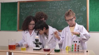 Kafkasyalı öğrenci kimyasal çözüm hazırlarken, yetenekli çocuklar mikroskop altında bakıyorlar. Profesyonel öğretmen, tahtada otururken deney yapıyor. Pedagoji.