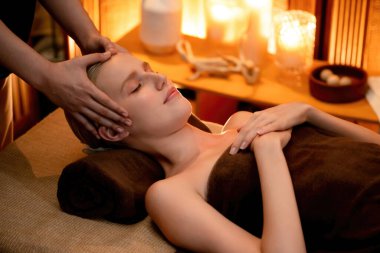 Beyaz kadın stres önleyici kafa masajı yapmaktan ve lüks otel veya otelde sıcak mum ışığında yüz güzelliği eğlencesi yapmaktan zevk alıyor. Sessiz.