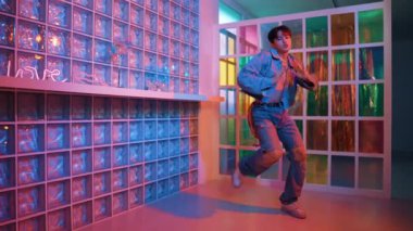 Çekici Asyalı sanatçı parlak neon ışıkta adım atıyor. Kameraya özgüvenle bakarken serbest stil müzikle dans eden yakışıklı break dans. Profesyonel hippi rahatla. Mutluluk.