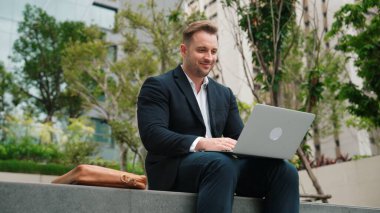 Yetenekli erkek lider Green City 'deki yatırım verilerini analiz ederken aynı zamanda dizüstü bilgisayarını kullanarak telefon gönderme raporu üzerinde çalışıyor. Parkta ya da şehir merkezinde otururken yatırımcı görünümlü mutlu pazarlama planı. Urbane.