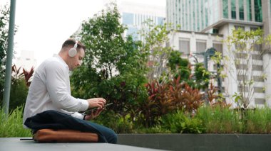 İş adamı, takım elbisesini çıkarırken ve Green City 'de müzik yaparken rahat müzik dinlemek için kulaklığını takıyor. Telefon çalarken canlı şarkıyla kulaklık dansı yapan bir menajer. Arkadan bak. Urbane.