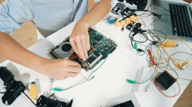 Masadaki elektronik aletle ana kartı tamir eden çocuğa yakın çekim. Elektronik teçhizatla lise öğrencilerinin elektrik panosunun en üst görüntüsü, kablo aletleri masanın etrafına saçılmış. Öğretim.