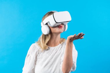 VR gözlüklü, elinde bir şey tutarken ayakta duran ve mavi arka planda duran beyaz bir kız. Görsel gerçeklik dünyasını birbirine bağlayan kadın holograma üflüyor ve bakıyor. Kısıtlanma.