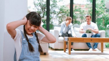 Stresli ve mutsuz genç kız köşeye kıvrılıp kulaklarını kapatarak arka planda ebeveyninin tartışmasını engelliyor. Evde aile içi şiddet ve travmatik çocukluk depresyona dönüşür. Eşzamanlama