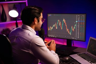 Akıllı tüccar işadamı, karanlık oda gecesinde neon ışıklı ofisteki arama pazarında yüksek kârla ekranda bilgisayar ve bilgisayar üzerinde dinamik borsa yatırımları üzerinde yoğunlaşıyor. Tahmin et..