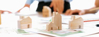 Profesyonel mimar mühendis takımı toplantı masasında ahşap blokla ve etrafa saçılmış planlarla mimari projeyle ilgili tartışır. Tasarım ve işbirliği konsepti. - Yakın çekim. Tanımlama.