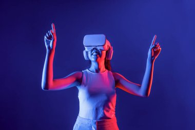 Siberpunk neon ışıklı cihazlarla çevrili zeki bir kadın metaevrene bağlı VR kulaklık takıyor, gelecekçi siber uzay teknolojisi. Sanal objeyi işaret eden bir kadın. Halüsinasyon.