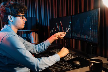 Genç yatırımcı hisse senedi tüccarı internetteki mevcut pazar grafiğinin çekici dinamik döviz kuru ekranlarıyla karşılaştırarak modern ofisteki finans grafik monitörünü işaret ediyor. Toplayıcı.