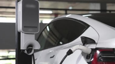 Şehir merkezindeki kapalı otoparkta yavaş çekimde EV elektrikli araba şarj oluyor. Şehir merkezinde sürdürülebilirlik yeşili, yeniden şarj edilebilir elektrikli araç iç organları.