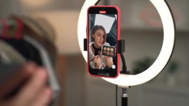 Arka plan etkileyicisi, vlog video gözden geçirme makyaj primi sosyal medya ya da blog kullanarak akıllı telefon yayınıyla canlı çekim yapıyor. İnternetteki pazarlama kaydı için kozmetik stüdyosu ışıklandırması olan kız.