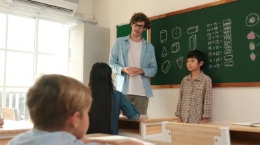 Öğrenci sınıfın önünde duruyor ve beyaz bir öğretmen öğrenciye bakıp çocuğu cesaretlendirirken kendini sınıfa tanıtmaya başlıyor. Çeşitli çocuklar oturur ve oğlanlara bakarlar. Pedagoji.