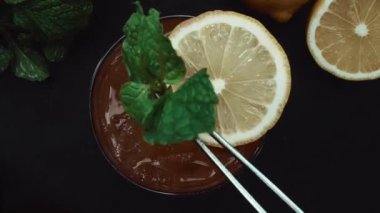 Makrografi, bir dilim limon ve taze naneyle süslenmiş Tekila Sunrise kokteyli, dramatik bir siyah arkaplan üzerine kurulmuş. Yakın çekim kokteylin canlı renklerini yakalar. Geliştirilebilir.