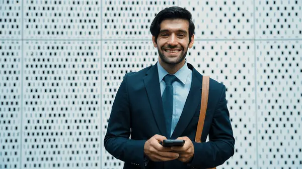 Portrait image of successful young business man looking at camera while hold phone with white background. Attractive caucasian investor or project manager standing at building. Close up. Exultant.