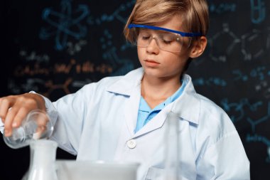 Laboratuvardaki sarışın çocuk laboratuvar önlüğü giyer ve STEM sınıfında kimya bilimi öğrenir. Öğrenci cam şişeye sıvı döker. Masaya bir sürü şişe koy. Etkinlik.