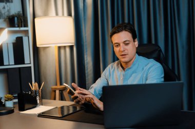 Akıllı iş adamı, müşterilerle veya yatırımcılarla iletişim kurmak için akıllı telefonuyla çalışır. Laptop ve tablet veritabanında geceleri mavi perde arkasında iş hedefiyle birlikte araştırma yapar. Bireysel.