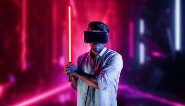 Lazer kılıcı tutan ve VR gözlük takan oyuncu. Beyaz adam, neon şatonun etrafında dikilirken görsel gerçeklik kulaklığı kullanıyor. Yenilik teknolojisi. Sapma.