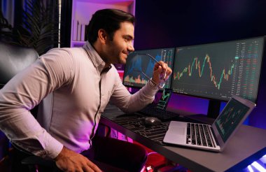 Akıllı tüccar işadamı, karanlık oda gecesinde neon ışıklı ofisteki arama pazarında yüksek kârla ekranda bilgisayar ve bilgisayar üzerinde dinamik borsa yatırımları üzerinde yoğunlaşıyor. Tahmin et..