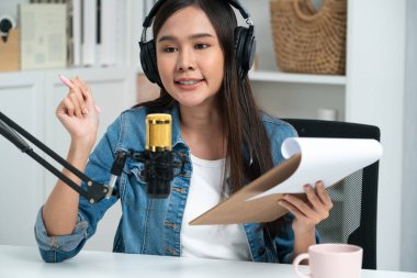 Sosyal medyada kulaklıkla canlı yayın yapan Asyalı sunucu modern stüdyoda yaşam koçluğu veya pazarlama dinleyicilerini selamlıyor. Taktik.