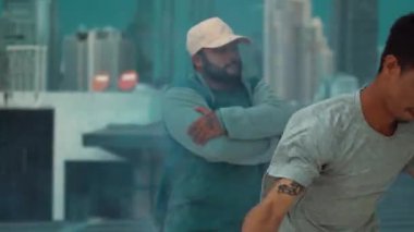 Bir grup çok kültürlü hippi çatıda işaret fişeği çalıyor. Zenci dumanı tutan çekici bir sokak dansçısı hip-hop müzik eşliğinde break dans yapıyor. Açık hava sporu 2024. Sokak dansı. hiphop.