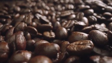 Kahverengi arkaplanlı kahve çekirdeği yığınını hareket ettiriyor. Kızarmış kahve tohumu ahşap masaya dağılır. Masaya kokulu organik kahve çekirdekleri koyun. Geliştirilebilir.