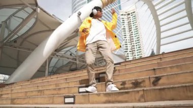 Asyalı şık bir adam alçak açılı kamerayla hip hop dansı yapıyor. Break dansçı, şehirde kulaklıktan müzik dinleyip dans ederken merdivenlerden çıkıyor. Açık hava sporu 2024. Yumuşak bir şekilde..