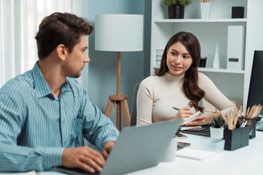 Akıllı yönetici dizüstü bilgisayarla yazarken iş analizi raporu için veri araştırma projesini modern ofis saatinde masa başında sorarak kadın iş arkadaşıyla konuşuyor. Varsayım.