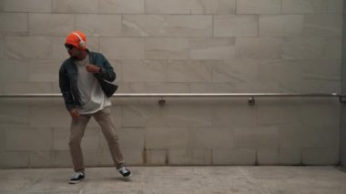 Asyalı akıllı hipster, kulaklık ve şık kıyafetler giyip hip hop şarkıları dinlerken gri arka planlı enerjik break dans gösterisi yapıyor. Açık hava sporu 2024. Hip hop hareketi. Yumuşak bir şekilde..
