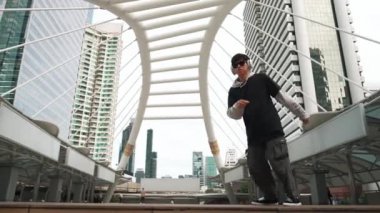 Genç Asyalı hippi şehir merkezinde insanların etrafında ayak izlerini gösteriyor. Şık bir sokak dansçısı B-boy ya da serbest dans eder. Açık hava sporu 2024. Break dans. Yumuşak bir şekilde..