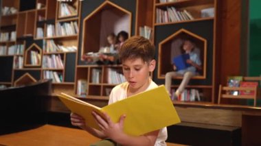 Bir grup zeki öğrenci kütüphanede otururken beyaz çocuk kitap okuyor. Çekici çocuk ders çalışıyor, çocuklar konuşurken romandan ya da kitaptan öğreniyor, eğitim hakkında sohbet ediyor. Etkinlik.