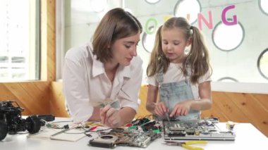 Genç, zeki, beyaz bir öğretmen öğrencilere elektronik kurulun bir parçasını öğretiyor. Uzman kız dijital elektrikli aletleri öğreniyor ve cips ve kablolarla ana kartı tamir ediyor. Etkinlik.
