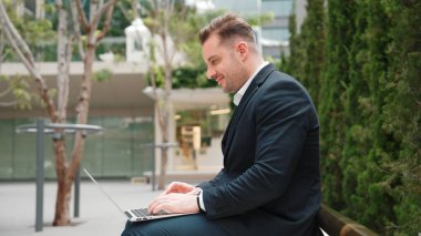 Green City 'de otururken bilgisayarla çalışan iş adamlarının yan görüntüsü. Akıllı yönetici bilgisayar yazma raporunu ve pazarlama stratejisini uzaktan kumandayla iş ekibiyle çalışırken kullanıyor. Urbane.