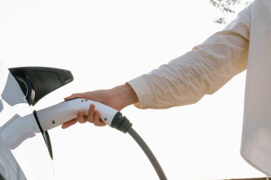 Genç bir kadın şarj aletini şarj istasyonundan elektrikli araba aküsünü şarj etmek için kullanmış. Sürdürülebilir çevre dostu seyahat konsepti için alternatif enerji ve şarj edilebilir EV araba. Yararlı