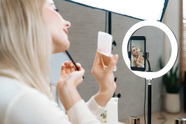 Sosyal medya için güzellik ve kozmetik video içeriği hazırlayan genç bir kadın. Güzellik blogcusu seyirciye güzellik hizmetini nasıl uygulayacağını ya da kamera karşısında takipçiyi nasıl izleyeceğini gösteriyor. Blithe