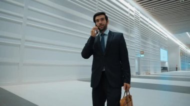 Profesyonel lider, işe başlama projesi için iş ekibini ararken ofise doğru yürüyor. Yakışıklı erkek lider toplantı odasına giderken telefonla pazarlama planı hakkında rapor veriyor. Sevinçli..