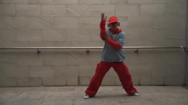 Yakışıklı koreograf gri arka planda sokak dansı yapıyor. Genç çekici erkek dansçı şık kıyafetler giyerken gösteri yapıyor. Hareketli bir adım. Uzayı kopyala Açık hava sporu 2024. Yumuşak bir şekilde..