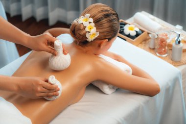 Sıcak bitkisel top spa masaj vücut tedavisi, masör kadın vücuduna nazikçe şifalı bitki torbası bastırıyor. Aromaterapi dinlenme sükuneti ve sükuneti kaplıca salonundaki atmosferi aydınlatıyor. Sessiz.