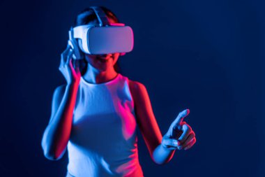 Siberpunk neon ışıklı cihazlarla çevrili zeki bir kadın metaevrene bağlı VR kulaklık takıyor, gelecekçi siber uzay teknolojisi. Sanal objeyi işaret eden bir kadın. Halüsinasyon.