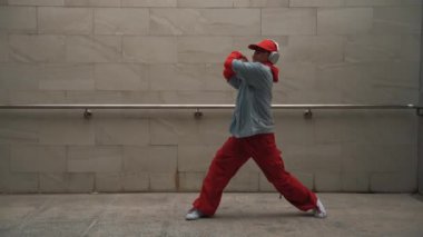Yakışıklı koreograf gri arka planda sokak dansı yapıyor. Genç çekici erkek dansçı şık kıyafetler giyerken gösteri yapıyor. Hareketli bir adım. Uzayı kopyala Açık hava sporu 2024. Yumuşak bir şekilde..