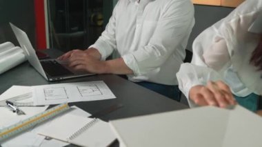 Bir grup mimar mühendis birlikte çalışıyor ve ofis tasarımı hakkında tartışıyorlar. Genç mühendis ev modelini ölçerken yönetici dizüstü bilgisayar kullanıyor. İş tasarımı konsepti. Yönlendirici.