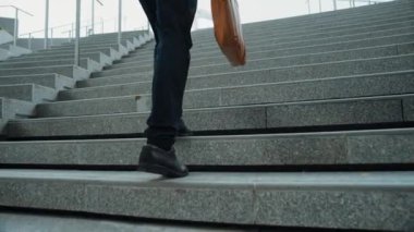 Akıllı bir iş adamının elinde çantayla merdivenlerden yukarı çıkışının en üst görüntüsü. Profesyonel proje yöneticisi merdivenlerden çıkıp işyerine gidiyor. Yeteneklerini arttırmak, terfi almak, seyahat etmek. Sevinçli..