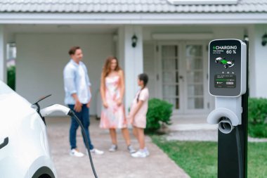 Bulanık arka planda, modern çevre ailesi için alternatif ve sürdürülebilir enerjiyle çalışan EV otomobil için ev şarj istasyonundan odaklanmış elektrikli araç şarj bataryası. Eşzamanlama