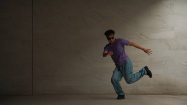 Zeki sokak dansçısı, gri arka planlı bir binada break dansçı hareketi yapıyor. Genç ve çekici koreograf enerjik ve aktif hareket ediyor. Açık hava sporu 2024. Yumuşak bir şekilde..