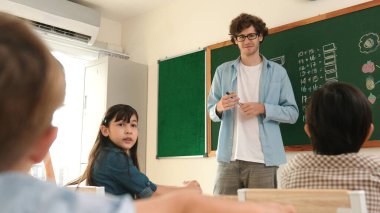 Matematik formülü veya teorisi ile karatahtanın önünde dururken sınıfın etrafına bakan profesyonel akıl hocası. Çeşitli ilköğretim öğrencileri matematik dersinde öğreniyor, çalışıyor ve oturuyor. Pedagoji.